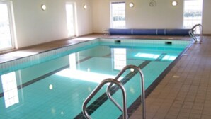 Una piscina interior con baldosas azules brillantes, barandillas de metal y suelo de baldosas.