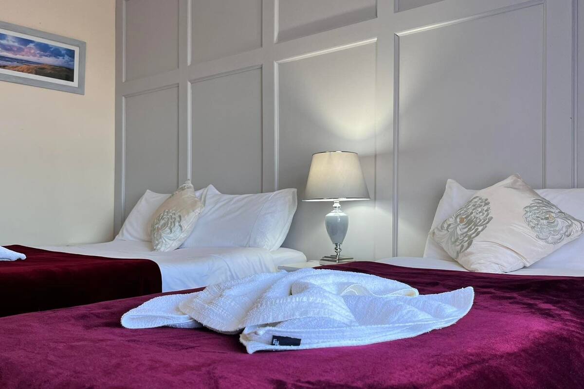 Quarto de hotel com duas camas, mesa de cabeceira com abajur e quadro na parede.
