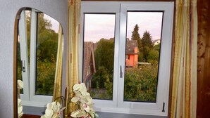 Ein Zimmer mit einem großen Fenster, einem Spiegel und einer Vase mit weißen Blumen.