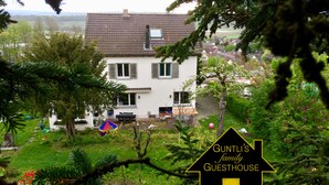 Ein Haus mit Ziegeldach, ein Garten mit Schaukel und ein Schild, das es als Pension kennzeichnet.