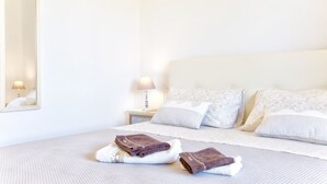 Una cama bien hecha con dos toallas dobladas, una lámpara de noche y un espejo en la pared.