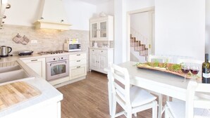 Una cocina moderna con armarios blancos, estufa a gas, microondas y comedor con mesa de madera y sillas blancas.