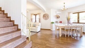 Un espacio habitable amplio con una escalera, una mesa de comedor con sillas y un gran reloj de pared.