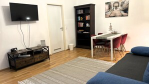 Una sala de estar moderna con un televisor de pantalla plana, un mueble de madera, una mesa de comedor con sillas rojas, una estantería y un cuadro en la pared.