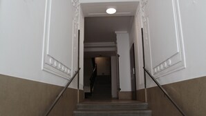 Una escalera con barandilla, paredes blancas con molduras decorativas y una sección inferior color beige.