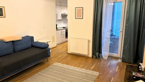 Una sala de estar con un sofá, un tapete estampado, una cocina al fondo y vistas a través de una puerta.