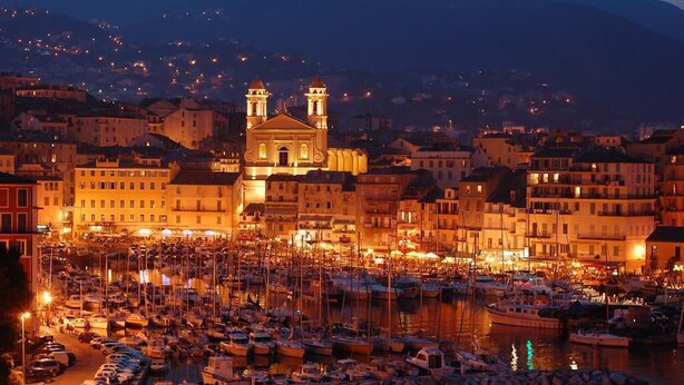 A marina with boats docked, a prominent church with two towers, and surrounding buildings.