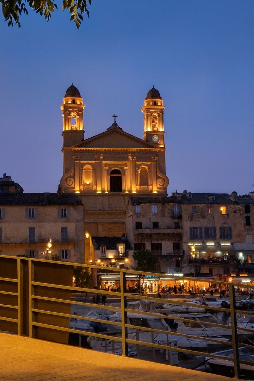 A church with two towers and a clock, surrounded by buildings and a marina with boats.