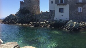 A coastal building with a stone tower and a white facade, situated next to clear blue water.