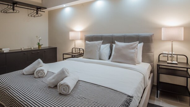 A hotel room with a large bed, two bedside tables with lamps, a dresser, and a wall-mounted towel rack. - Ancient Agora Industrial Suite (Thessaloniki)