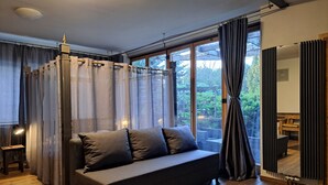 A modern living room with a sofa, large windows, and a view of the outdoors. - Champêtre Park View Apartments (Riga)