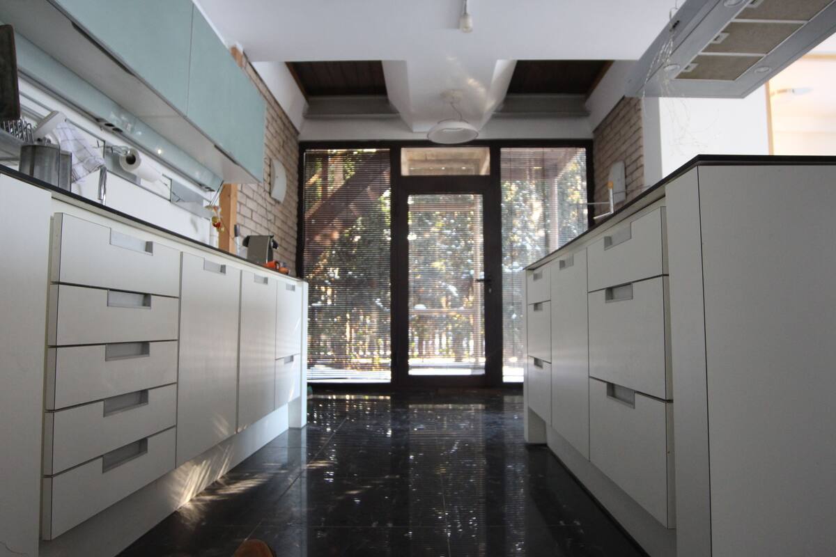 A modern kitchen with white cabinets, a black floor, and a large window with blinds.