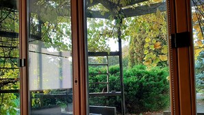 A conservatory with a glass door, a wooden bench, and a stone bench. - Champêtre Park View Apartments (Riga)