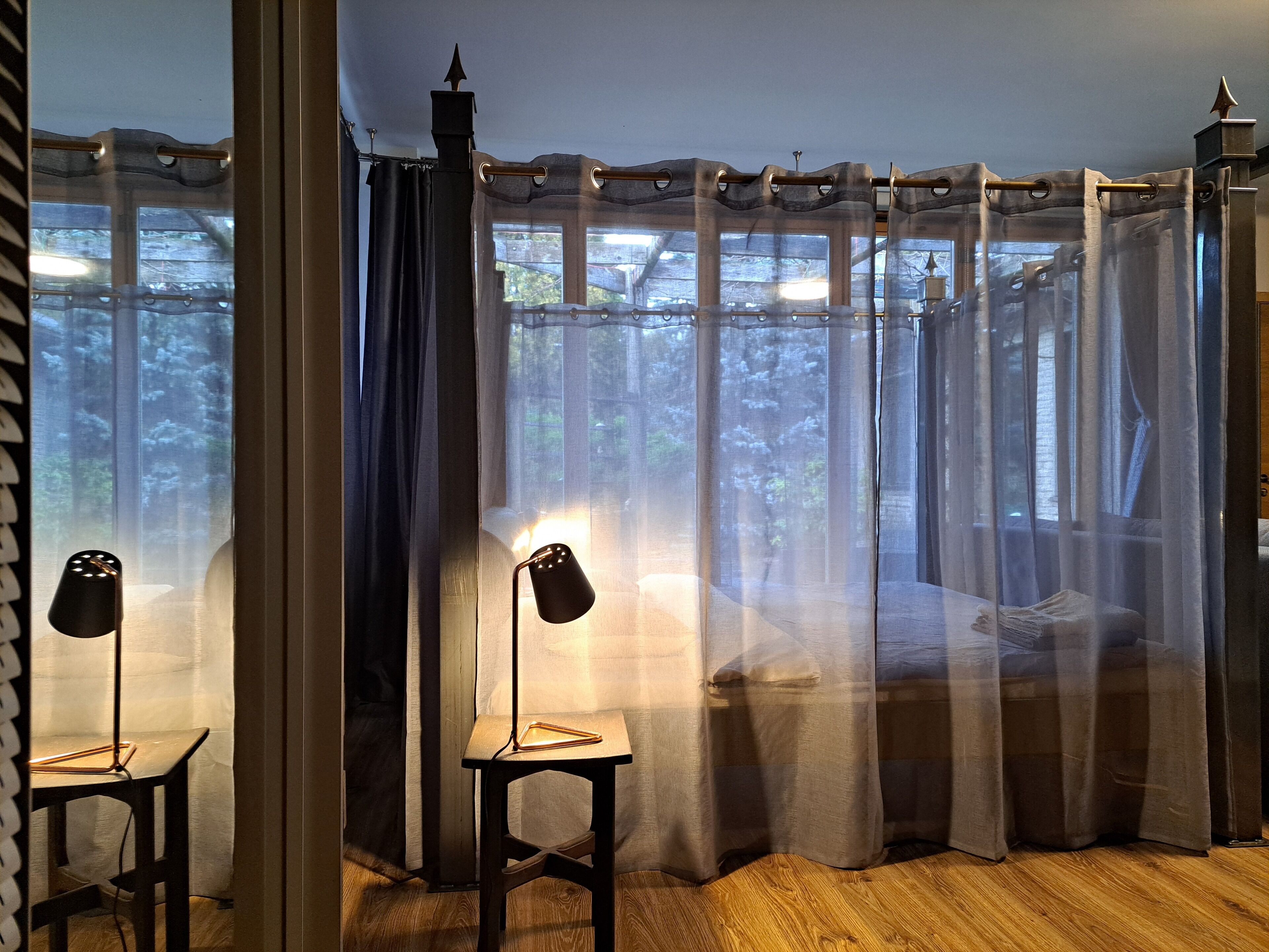 A bedroom with a bed, two chairs, a nightstand, and sheer curtains.