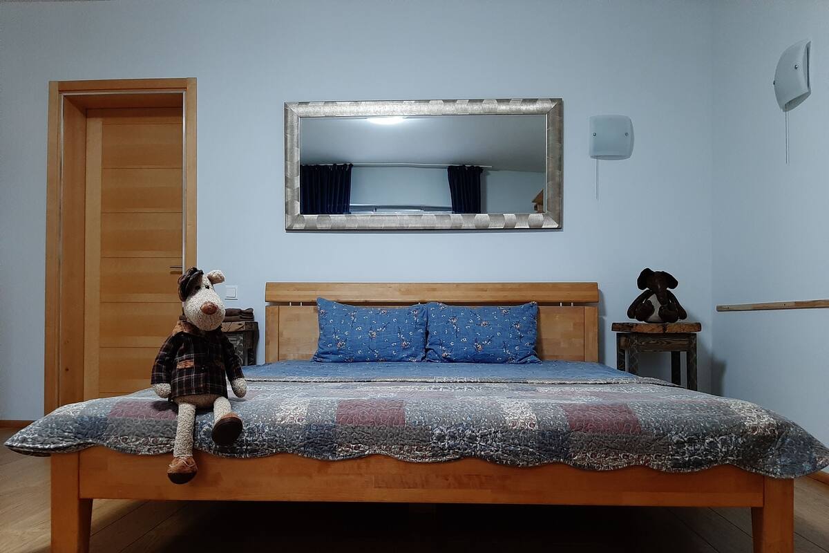 A bedroom with a wooden bed, a mirror above it, and a teddy bear on the bed.