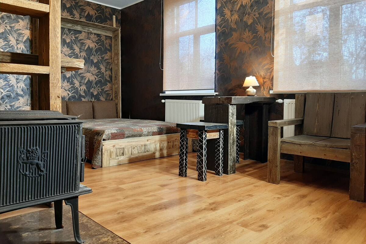 A room with a bed, a wooden table, a chair, a radiator, and a window with a view of trees.