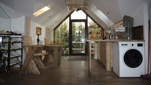 A kitchen with a washing machine, wooden furniture, and a view through a large window. - Champêtre Park View Apartments (Riga)