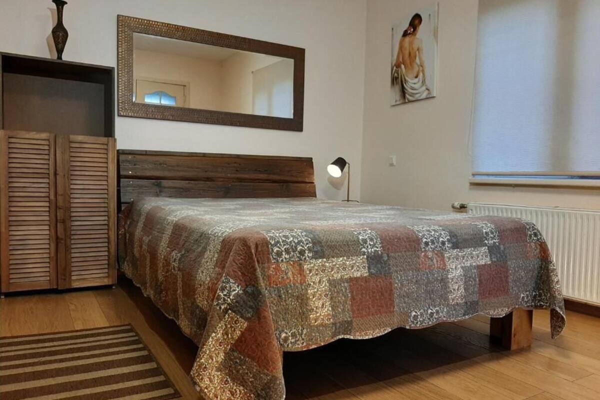 A bedroom with a wooden bed, a large mirror, a radiator, and a window with blinds.
