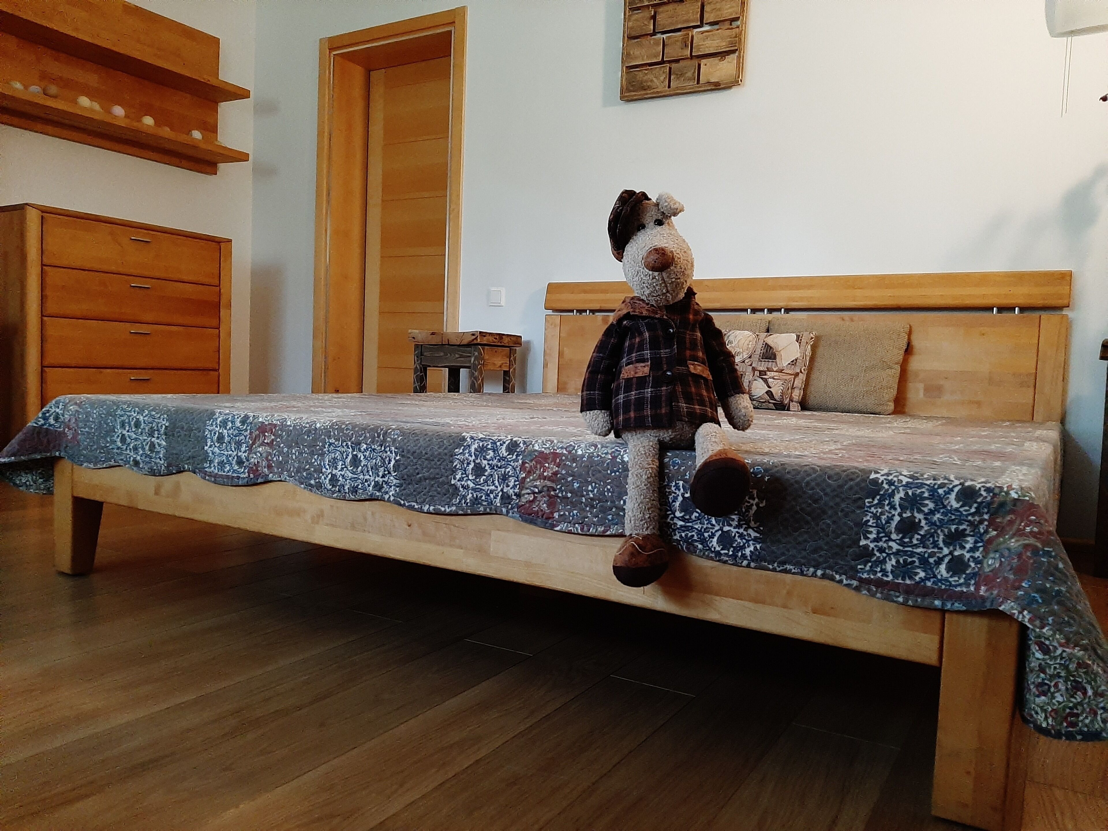 Un dormitorio con una cama de madera, una mesita de noche pequeña de madera, un aparador de madera y una estantería en la pared.