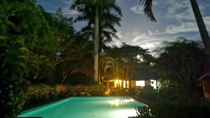 A swimming pool surrounded by lush greenery and palm trees, with a building in the background. - Explore Paradise-Palma Real cottage (Liberia)