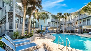 A pool area with lounge chairs and a pool, surrounded by a building with balconies and palm trees.