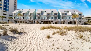 A beachfront hotel with multiple balconies, a sandy beach in the foreground, and a clear blue sky.