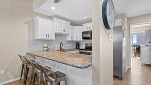 A kitchen with white cabinets, a granite countertop, stainless steel appliances, and a clock on the wall.