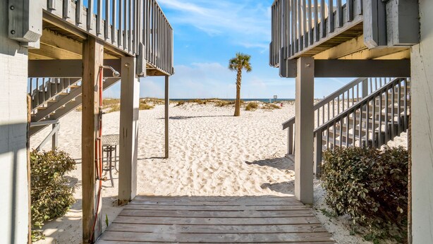 A wooden pathway leading to beach access with a palm tree and sandy beach in the background.