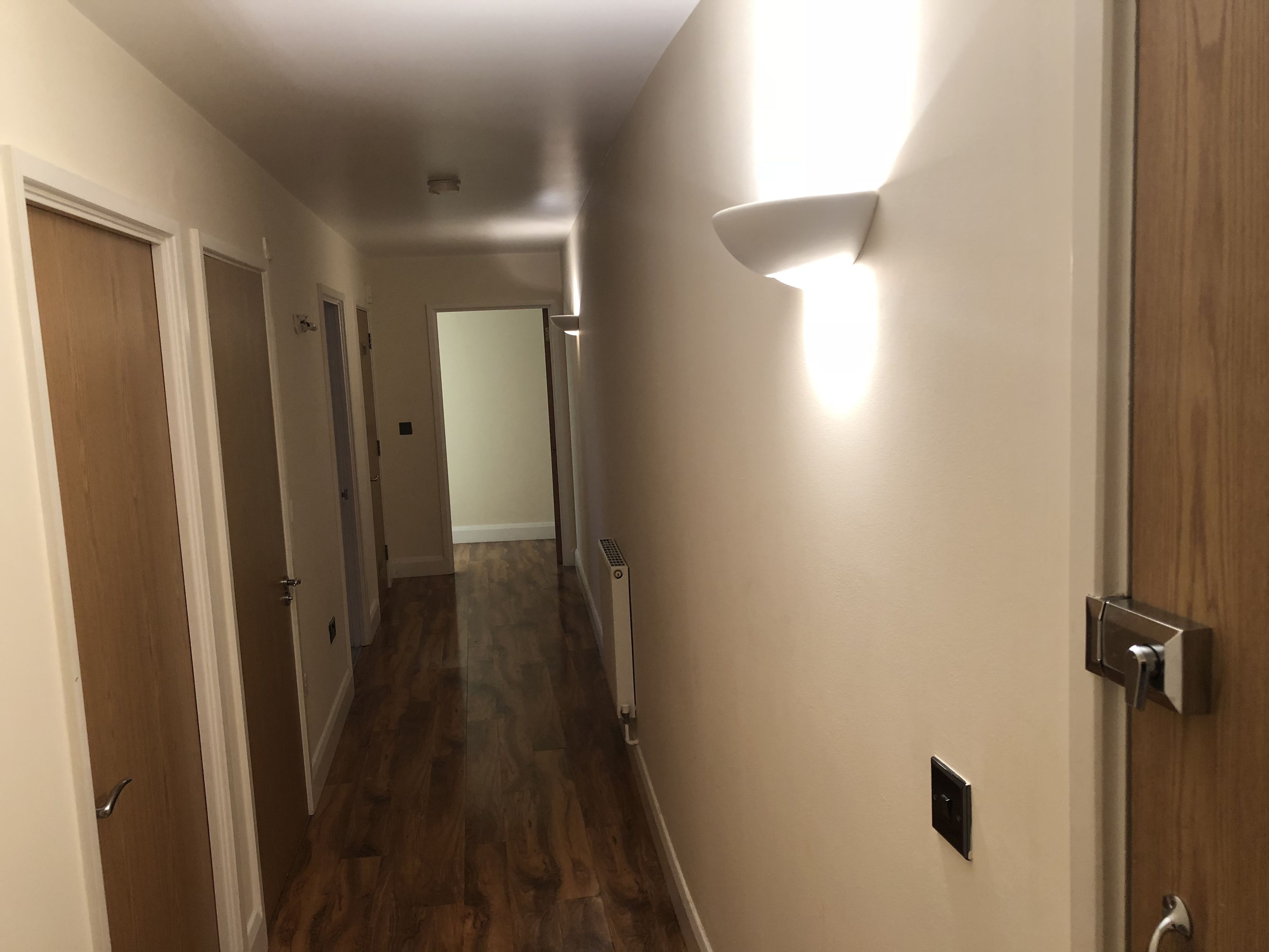 A hallway with wooden flooring, white walls, and a door on the right.
