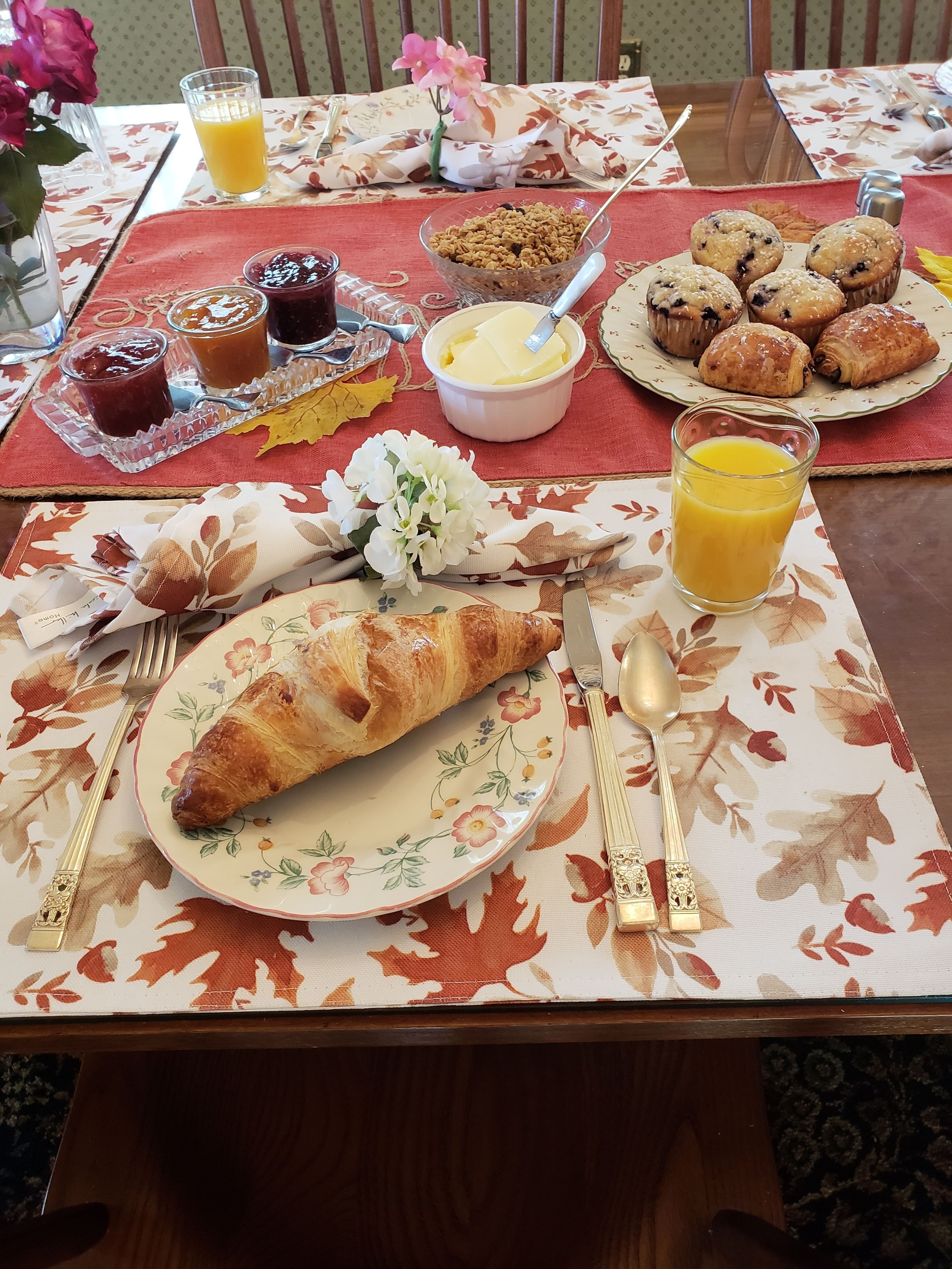 A breakfast setting with a croissant, muffins, and juice on a floral tablecloth.