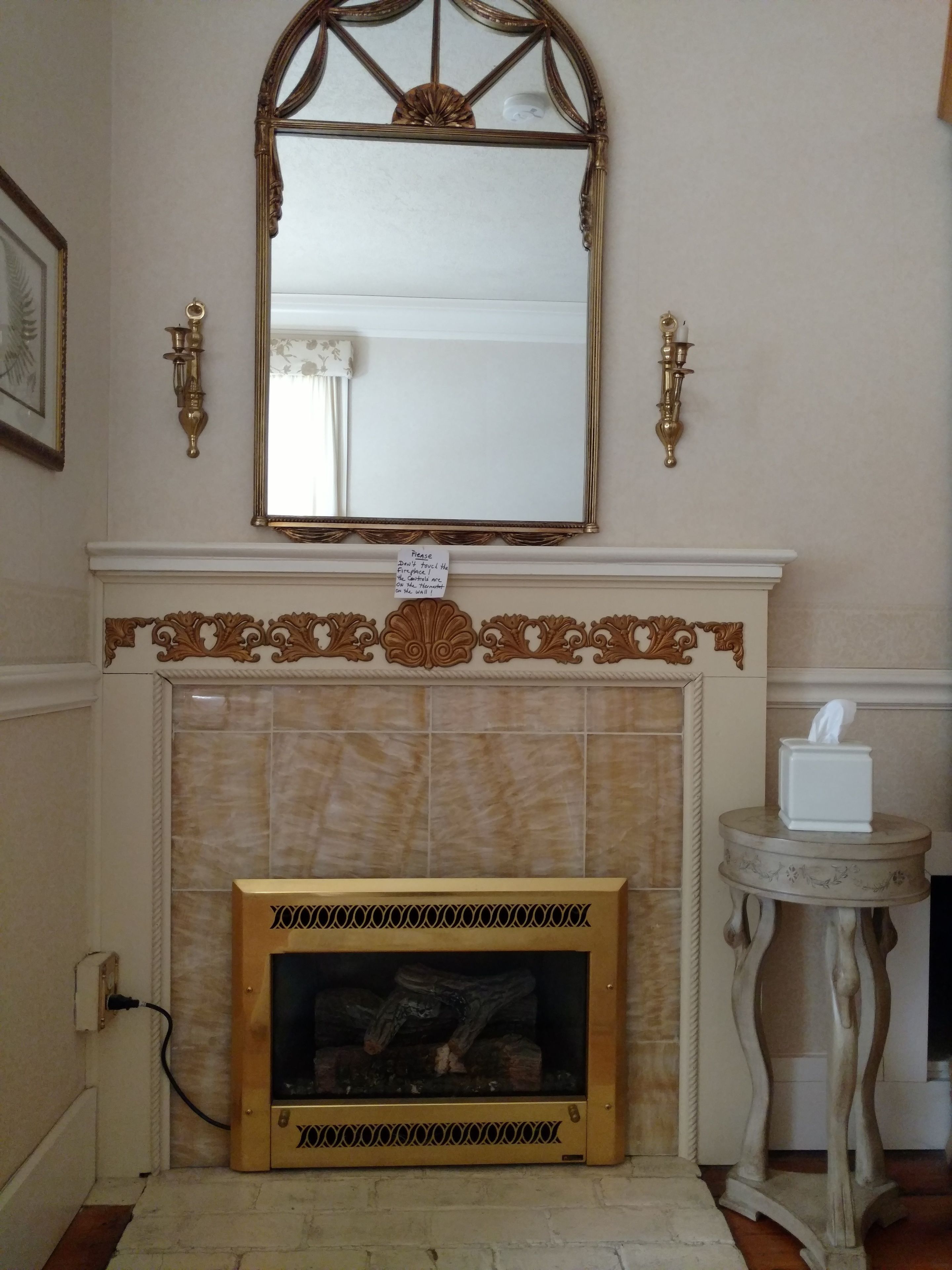 A fireplace with a mirror above it, a small table with a tissue box, and a sign on the fireplace.