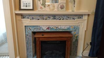 A fireplace with mosaic tile work, a framed picture, and a vase with a flower on the mantel.