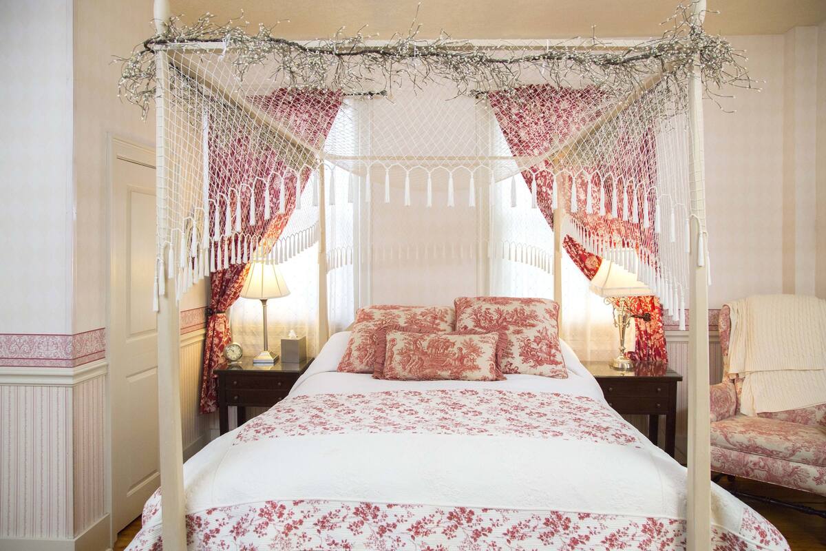 A four-poster canopy bed with floral bedding and a white canopy.