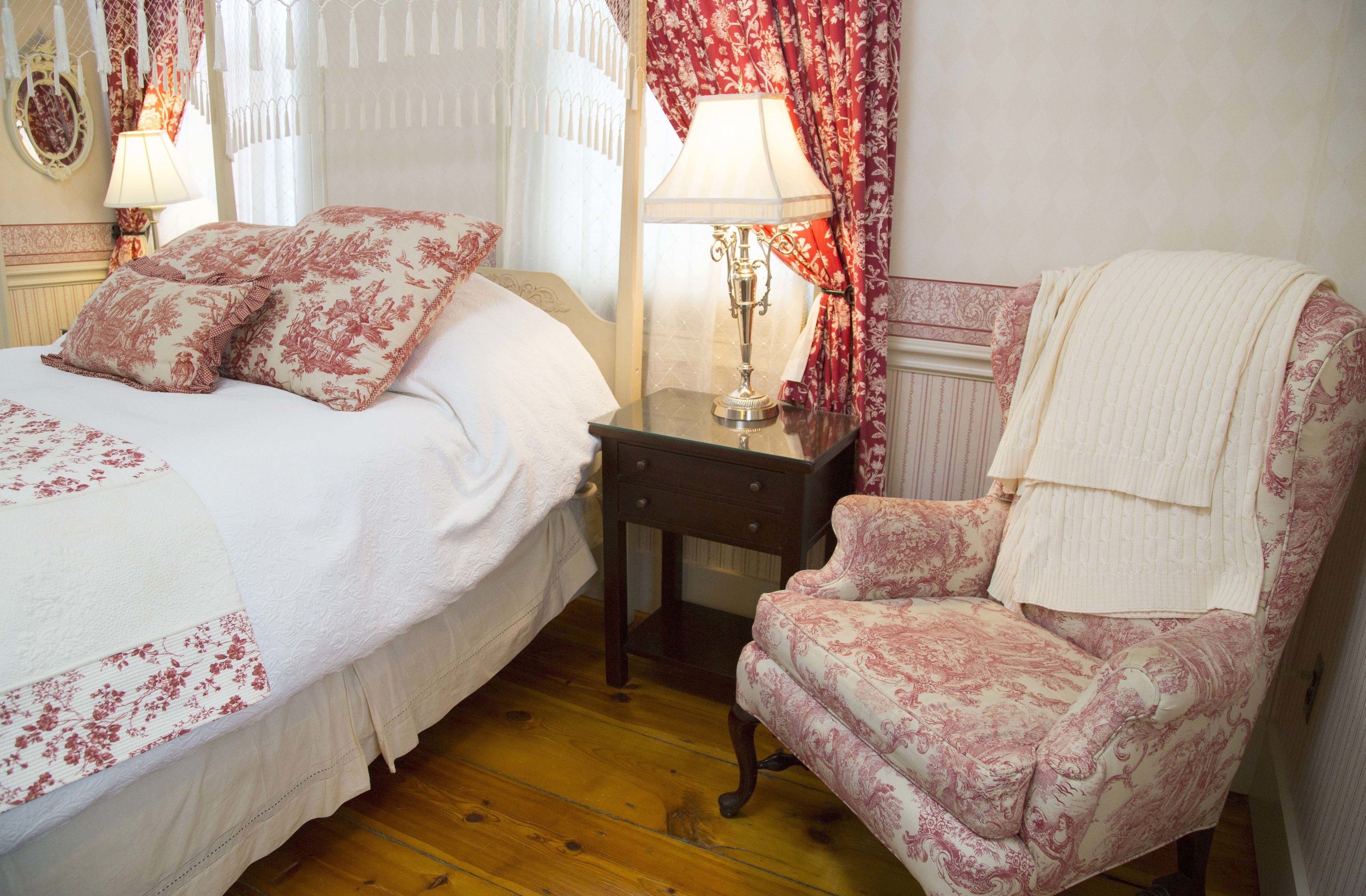 A bedroom with two beds, a nightstand with a lamp, a chair with a blanket, and floral-patterned bedding.