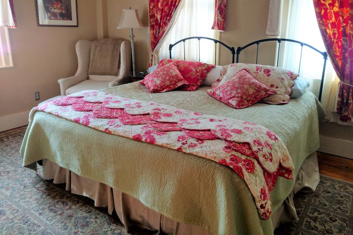 A bedroom with a bed, a chair, a lamp, and curtains.