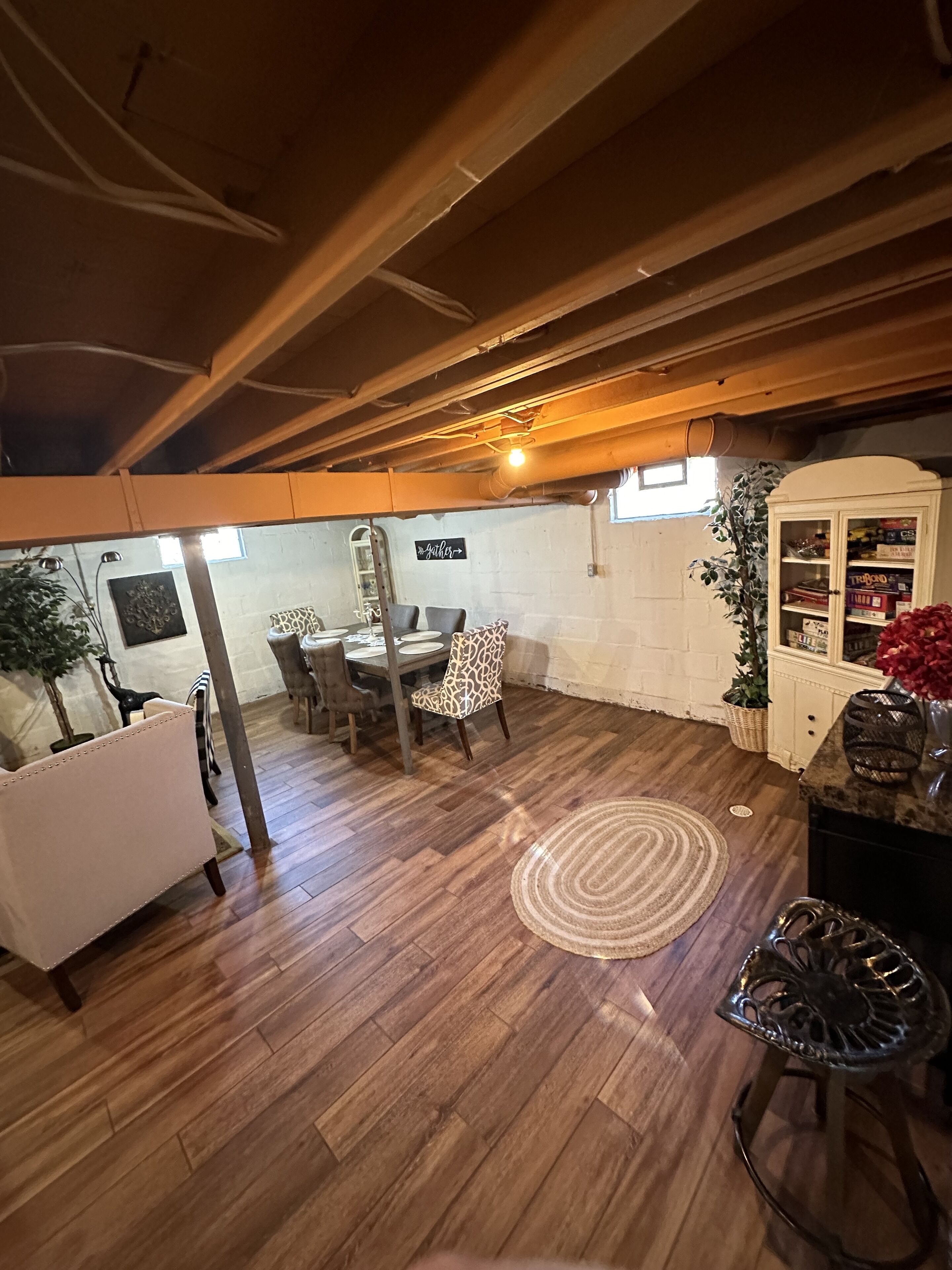 A dining area with a wooden ceiling, a dining table with chairs, a white cabinet with glass doors, and a potted plant.