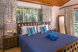 A bedroom with a large bed, two bedside tables with lamps, and a view of greenery outside.