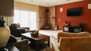 Een woonkamer met een open haard, een aan de muur bevestigde televisie en een gezellige zithoek.