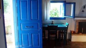 Een kamer met een blauwe deur, een eettafel met stoelen, een raam met uitzicht op groen, en een open haard.