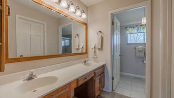 Une salle de bain dotée d’un grand miroir, de deux lavabos, de meubles en bois et d’un meuble-lavabo éclairé.