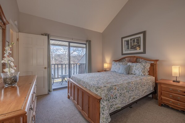 A bedroom with a bed, dresser, and a balcony with a view of trees.