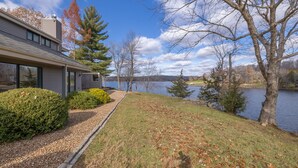 Una casa moderna con un ventanal grande con vistas a un lago, rodeada de árboles y un césped cuidado.