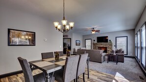 A dining area with a wooden table and chairs, a chandelier, and a fireplace in the background.