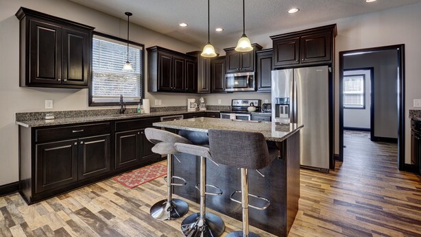 A modern kitchen with dark cabinetry, a central island with bar stools, stainless steel appliances, and pendant lighting.