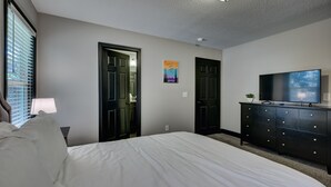 A bedroom with a bed, a dresser, a TV, and two doors.