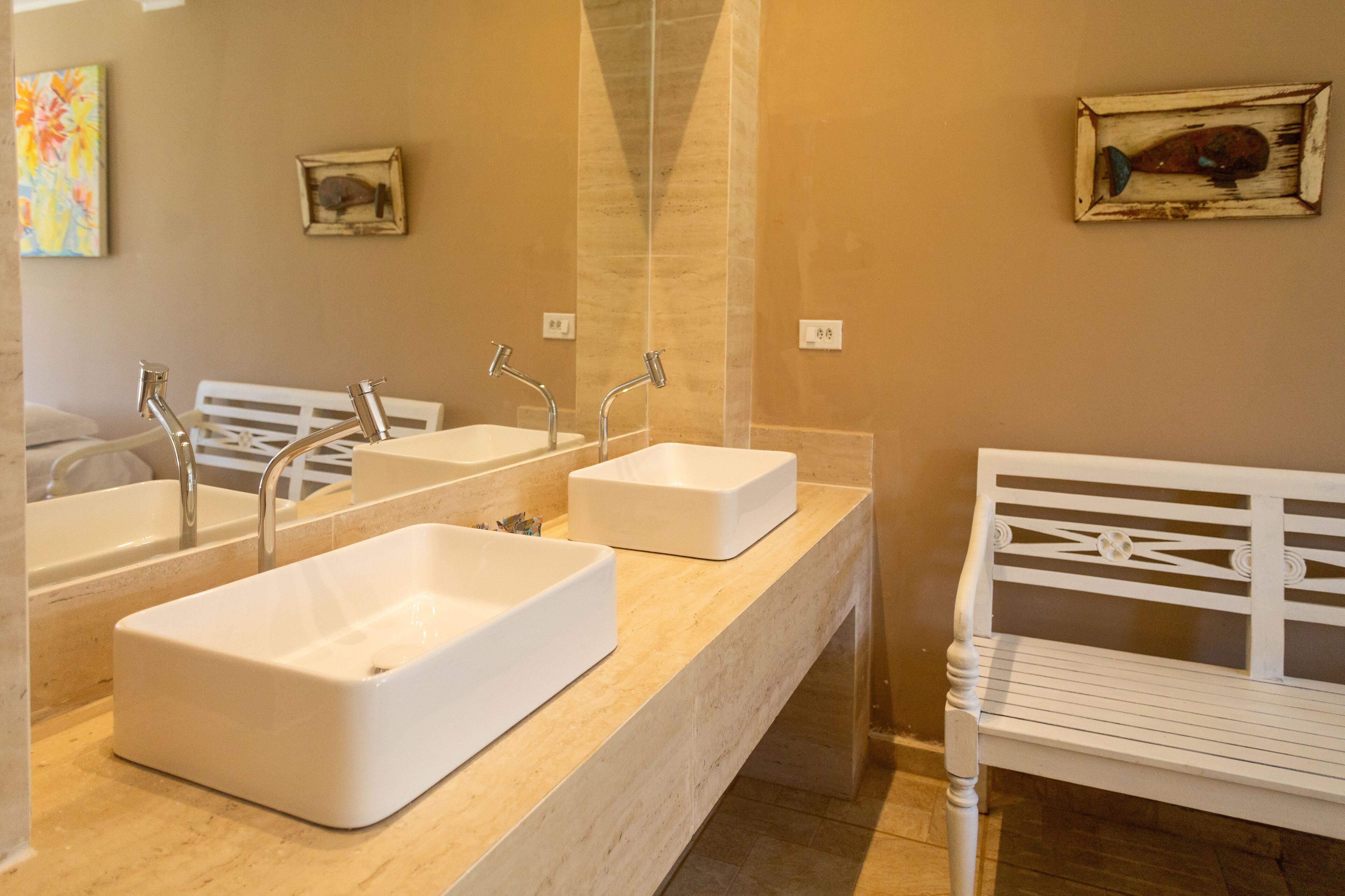 Ein Badezimmer mit zwei Waschbecken, einer Bank und Bildern an den Wänden.