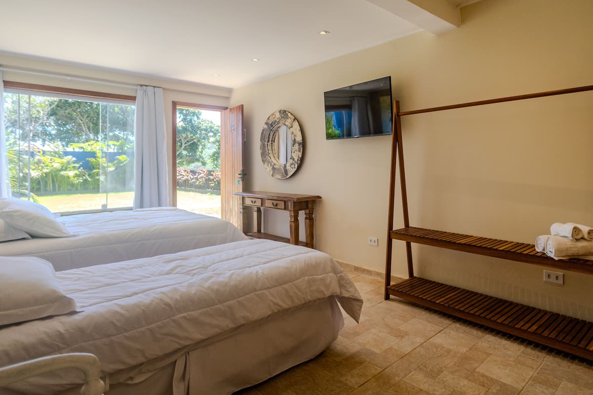 Habitación de hotel con dos camas, un televisor, un estante de madera con toallas y un espejo grande en la pared.