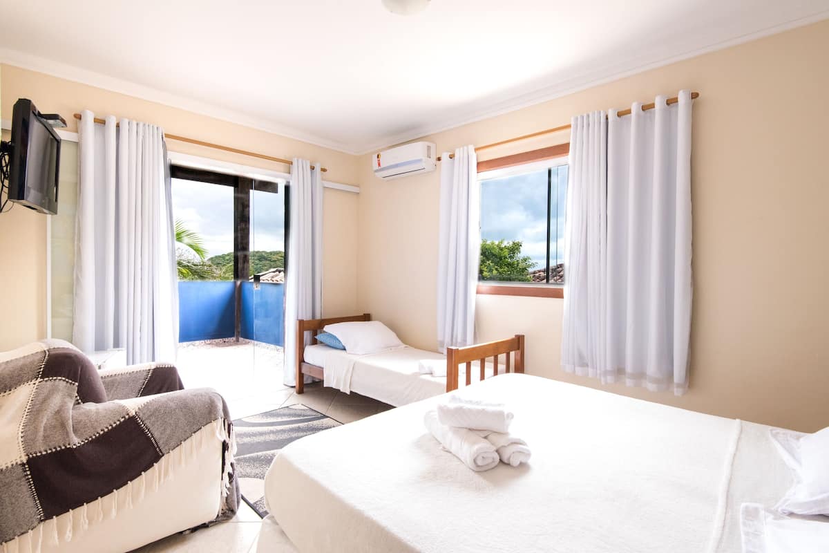 Una habitación de hotel con una cama, una silla, un televisor y un ventanal con cortinas.