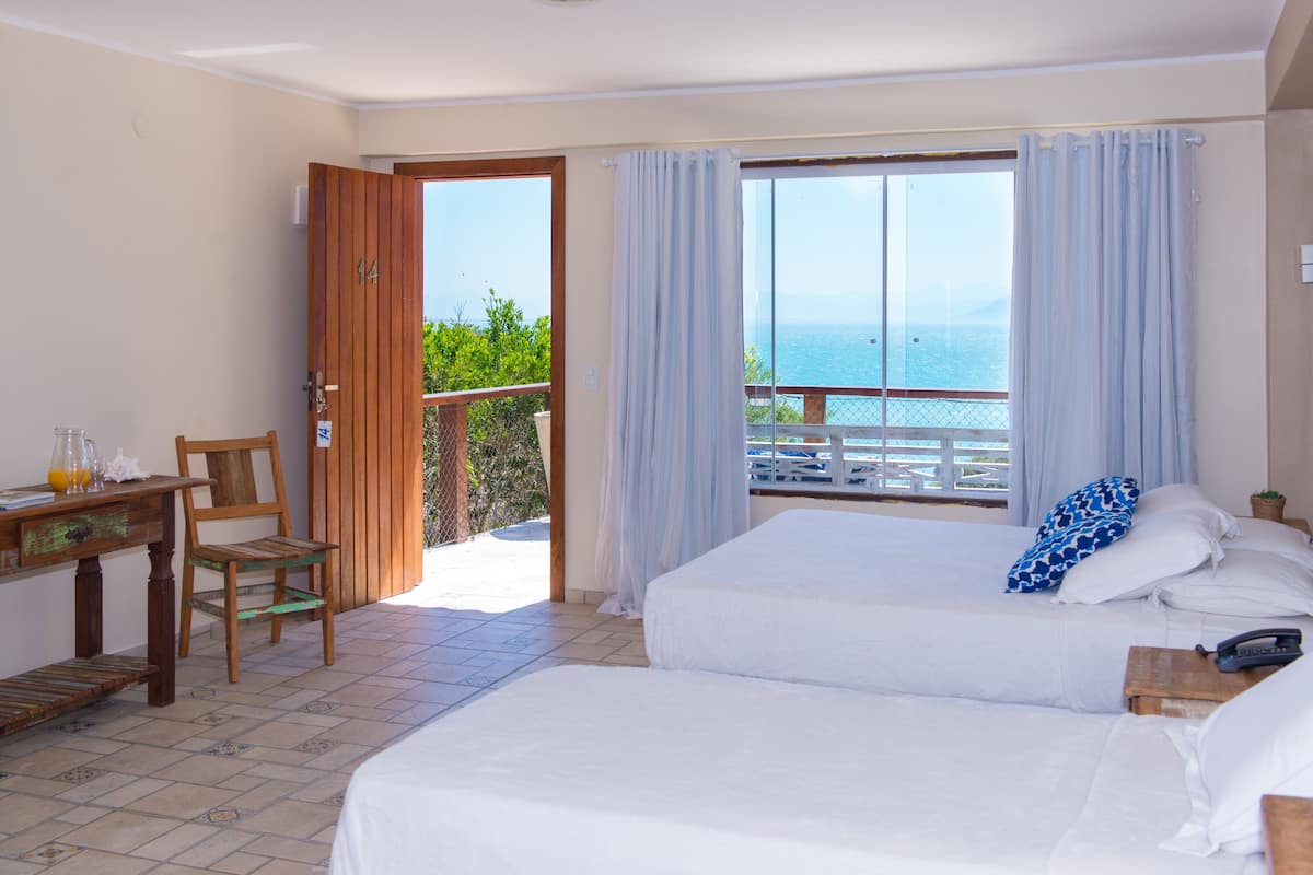 Una habitación con dos camas, un escritorio de madera, una silla y un balcón con vista al mar.