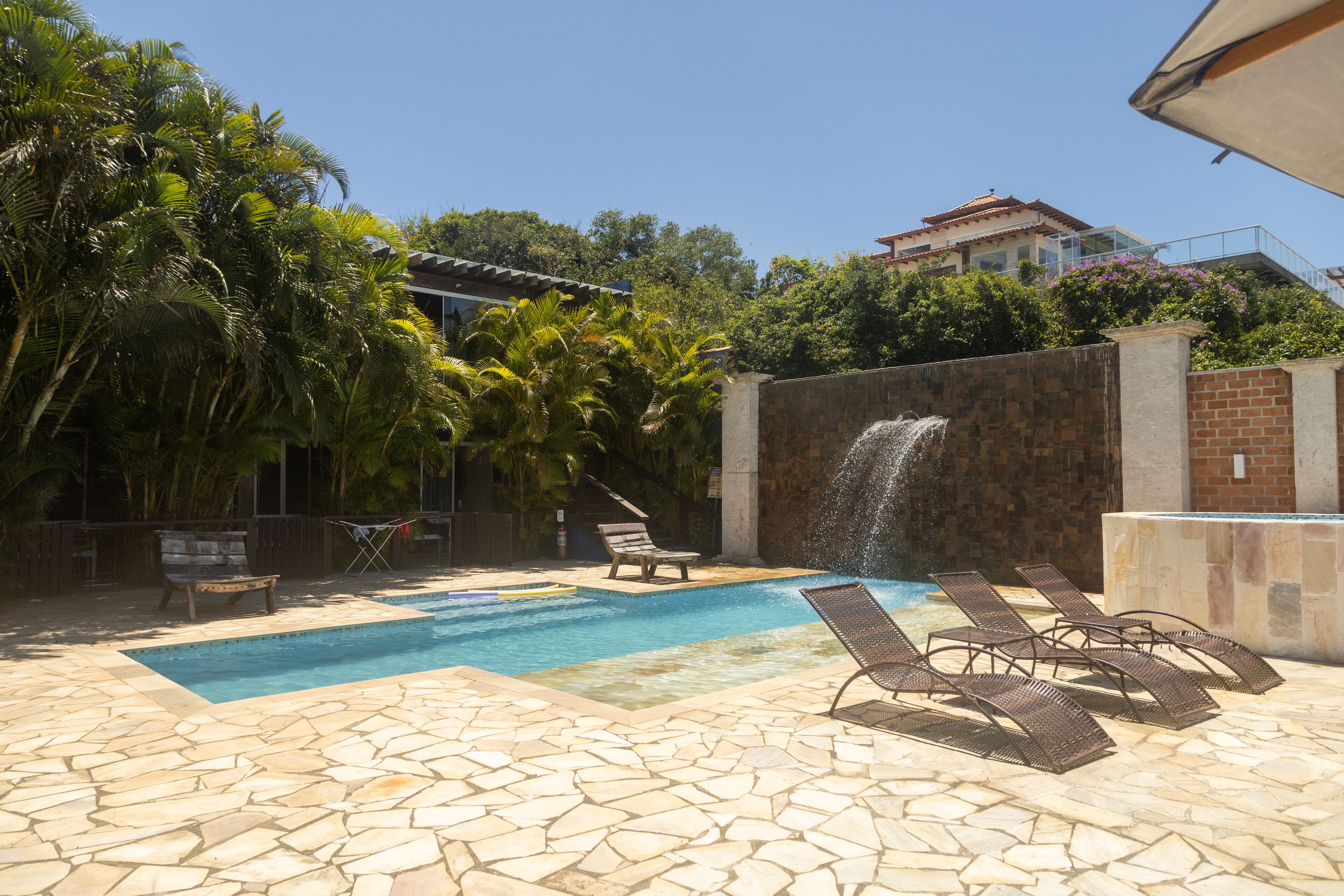 A swimming pool with lounge chairs, a waterfall feature, and a stone-tiled deck.